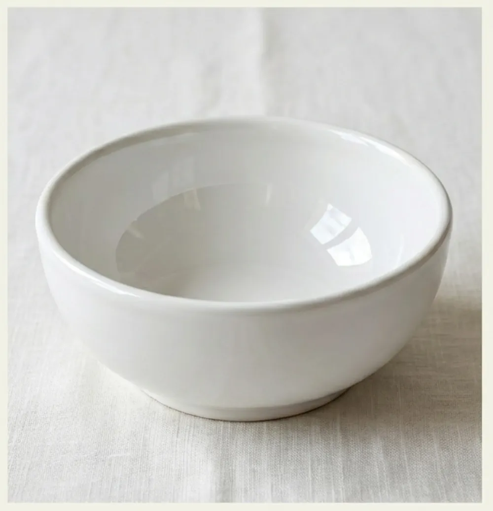 A plain white ceramic bowl on linen