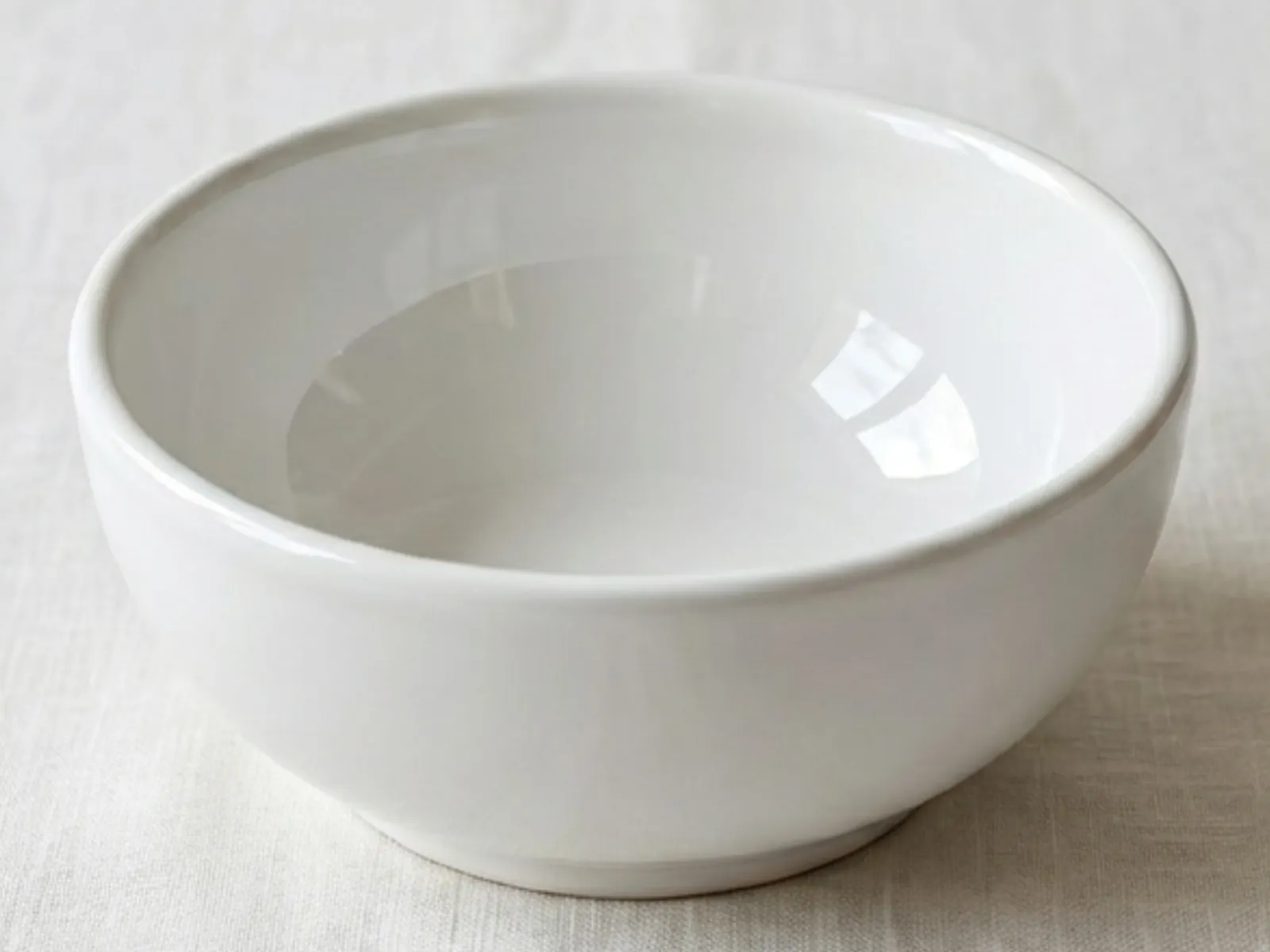 A plain white ceramic bowl on linen